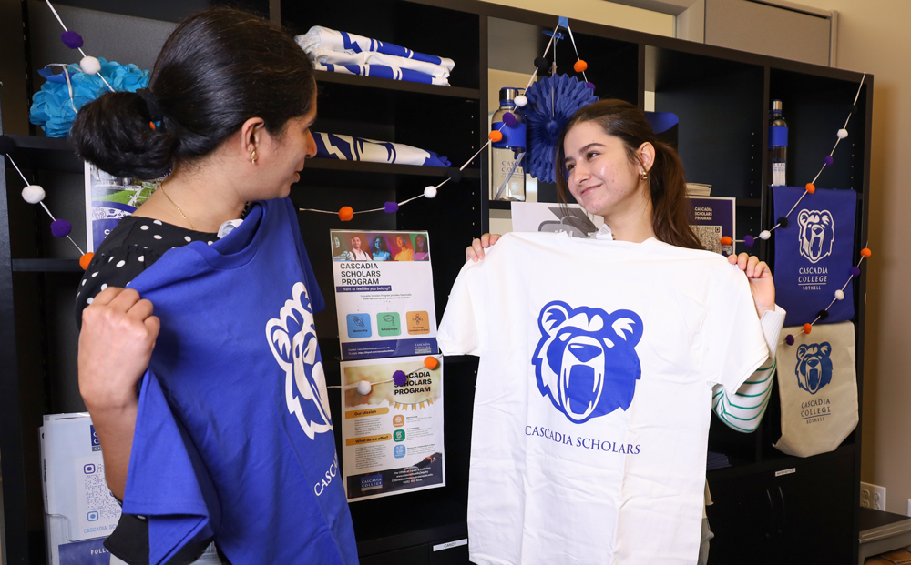 Two students holding Cascadia Scholars t-shirts up to themselves