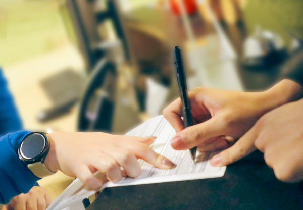 Board Policies A hand points to a white paper while another hand holds a pen, signing it.