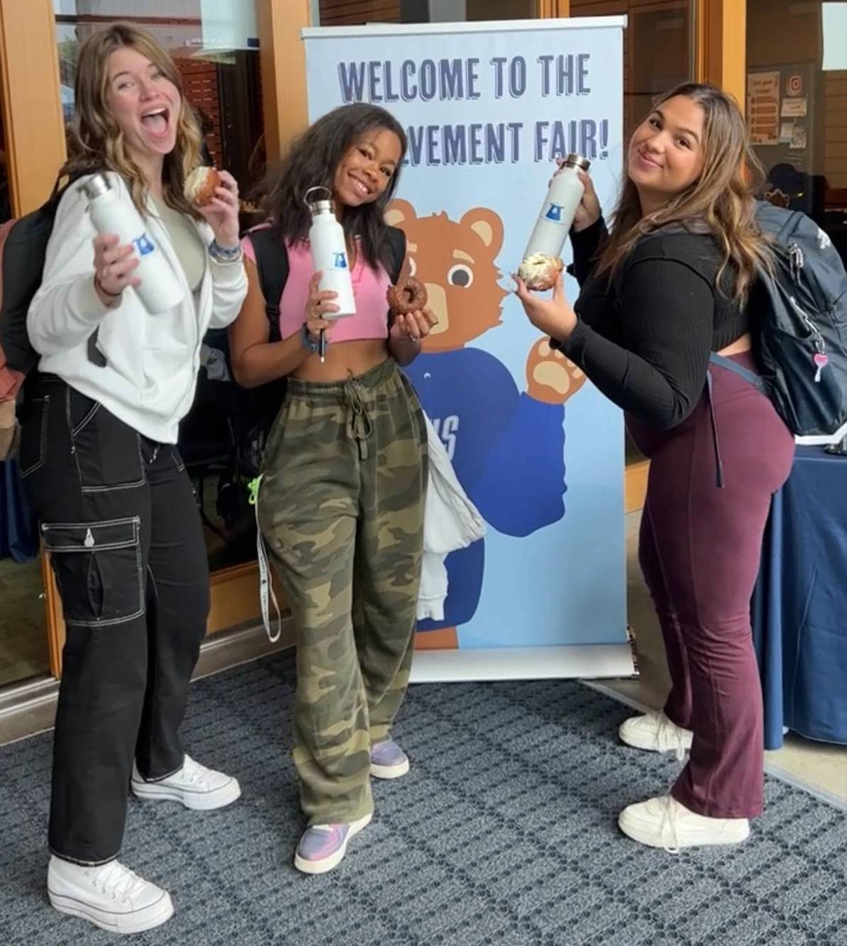 Student Life A diverse group of students smiling and waving in an outdoor setting, showcasing a positive and inclusive atmosphere.