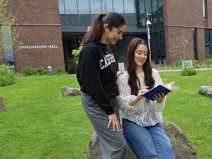 two students sitting on a rock outside of Innovation Hall reading a book