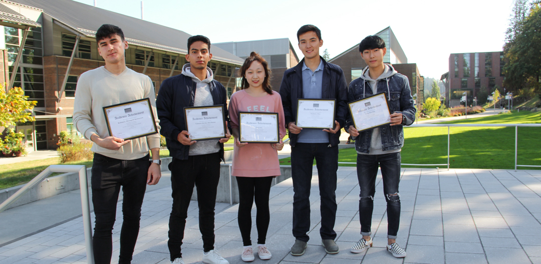 Students with scholarship award certificates five students in a line holding scholarship award certificates with Cascadia College campus in the background